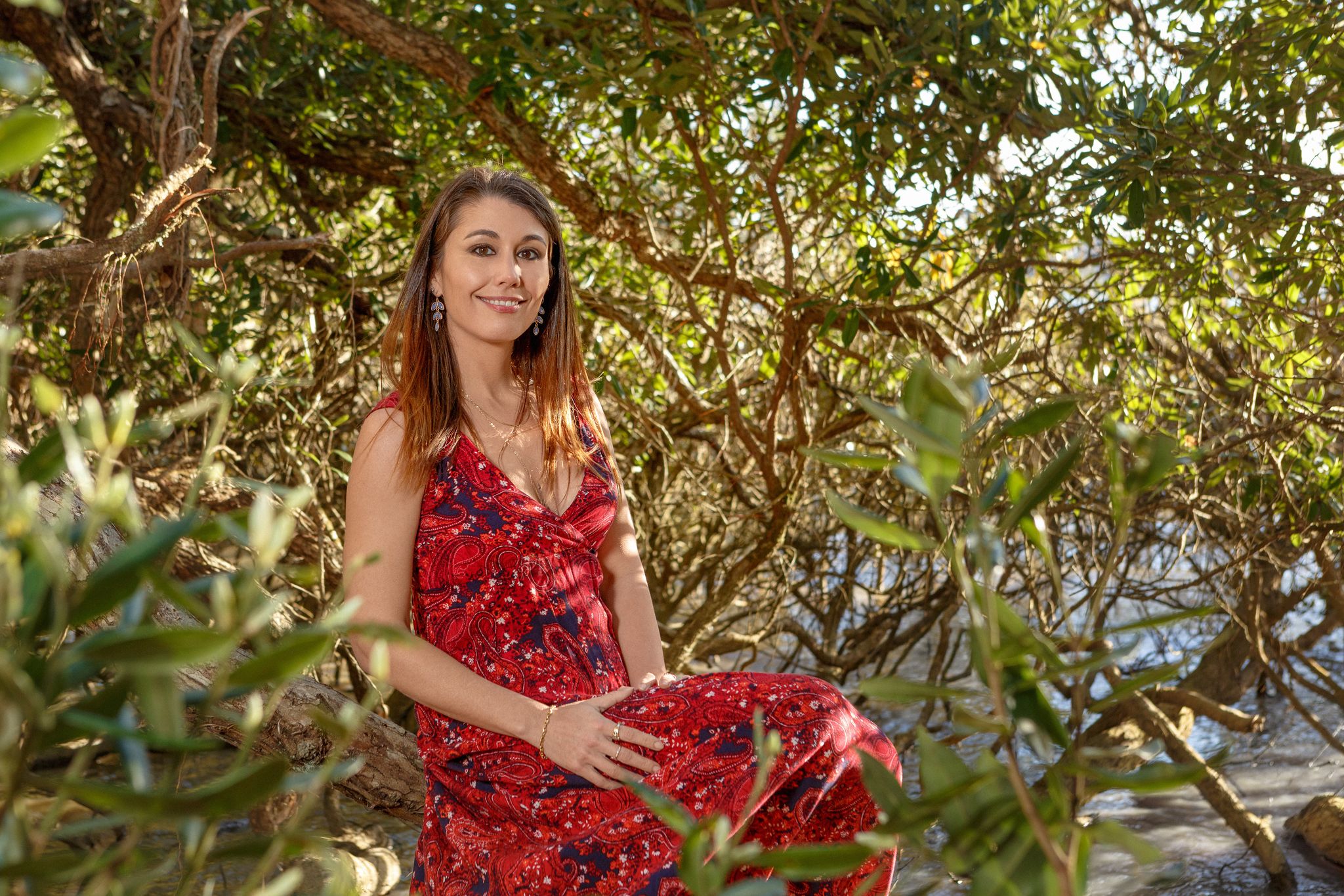 Alma in a red dress, sitting among green coastal trees