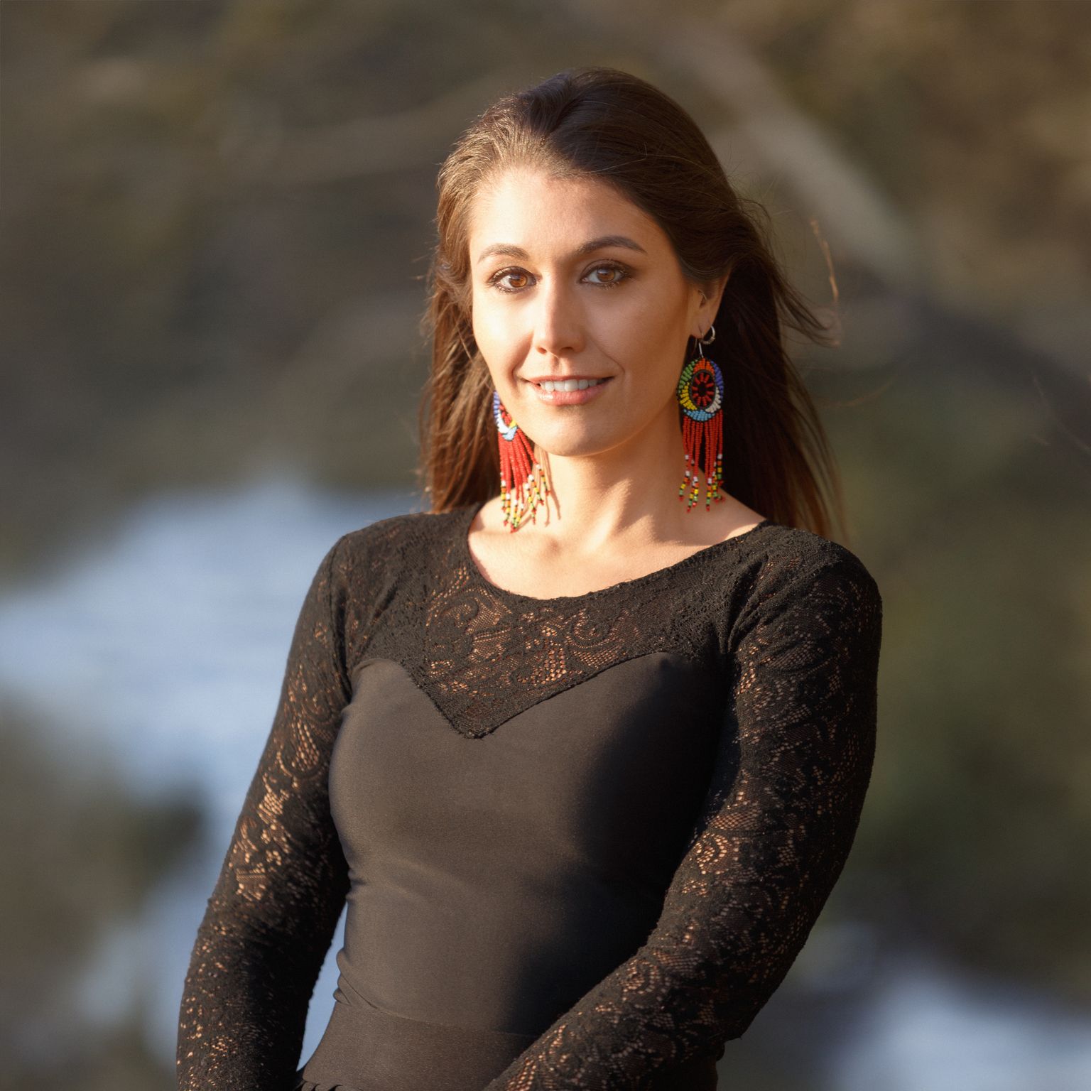 Alma, founder of Own Your Health, in a black lace top, standing by the water